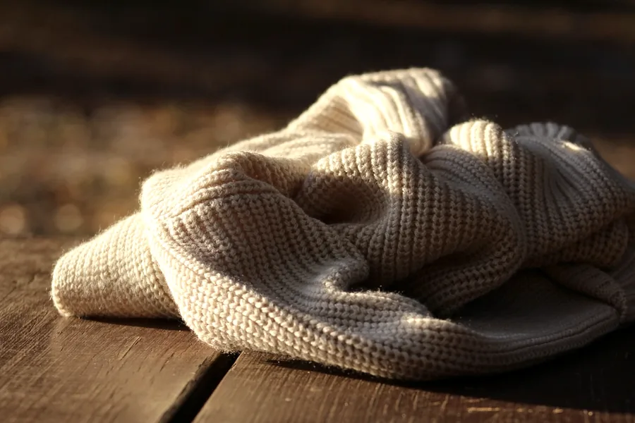 Cream knitted garment folded on a dark wooden table